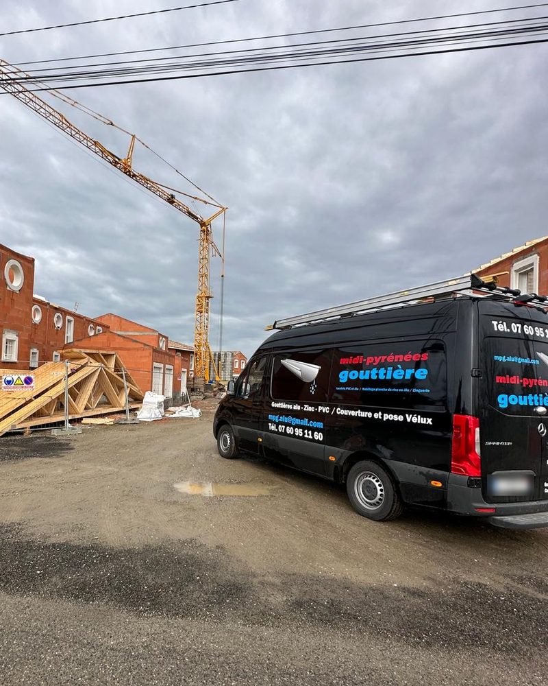 Le camion-atelier noir de Midi-Pyrénées Gouttière garé sur un chantier de maisons neuves, grue en arrière-plan