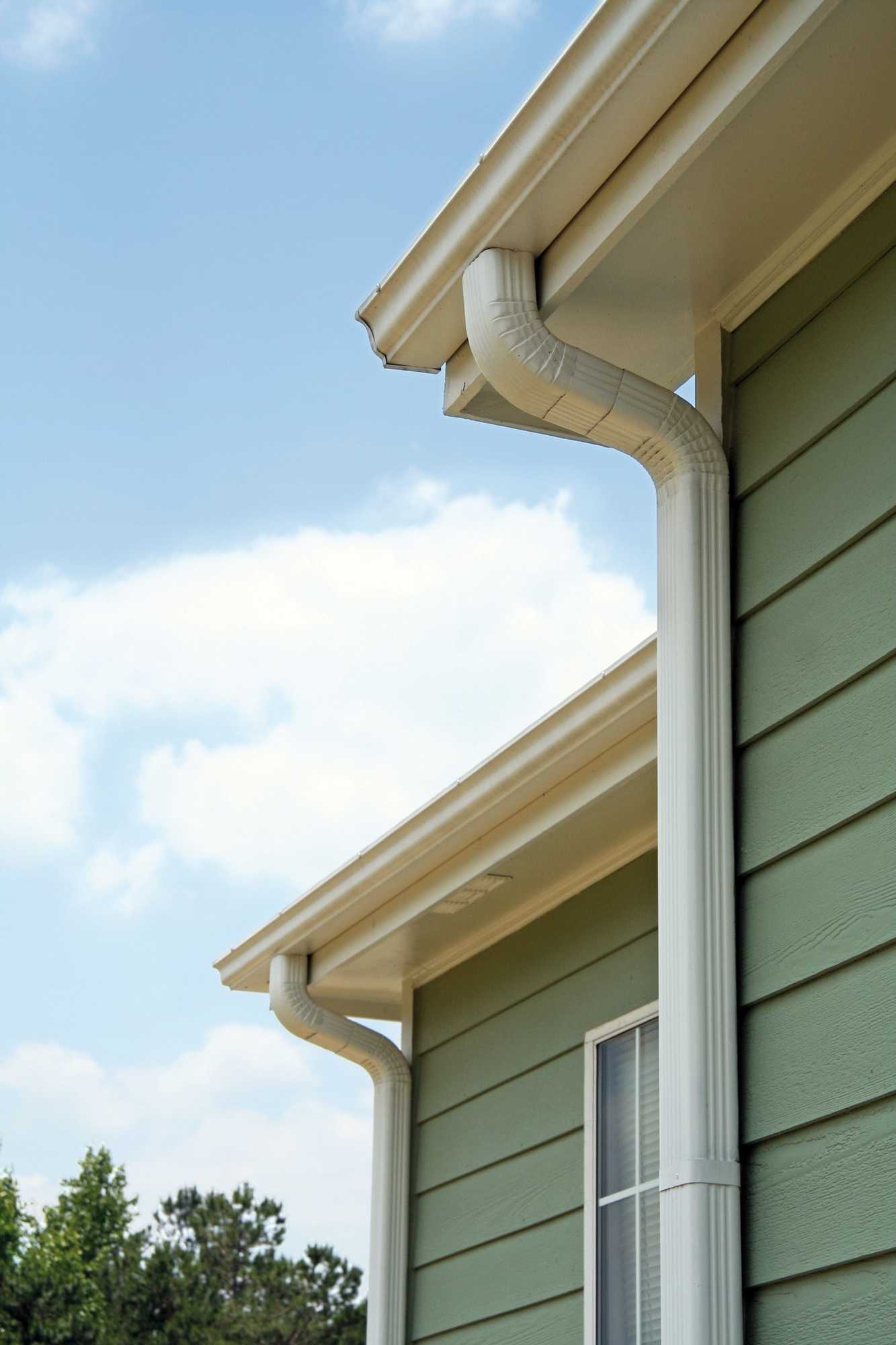 Gouttière et descente blanches posées sur une maison à bardage vert